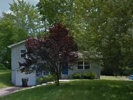 A white house with a red tree in front.