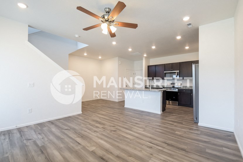 a renovated living room with a kitchen and a ceiling fan