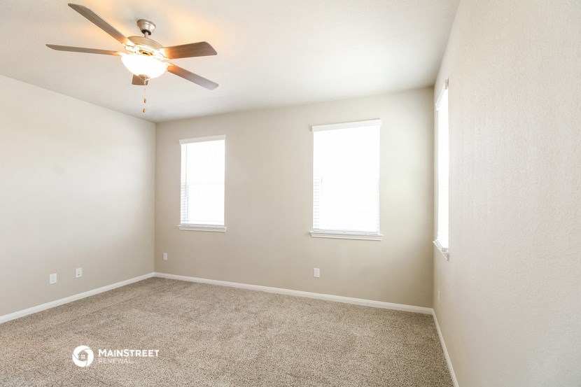 the spacious living room with ceiling fan and two windows