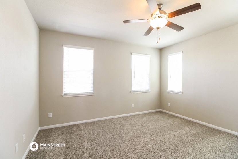 an empty room with a ceiling fan and three windows
