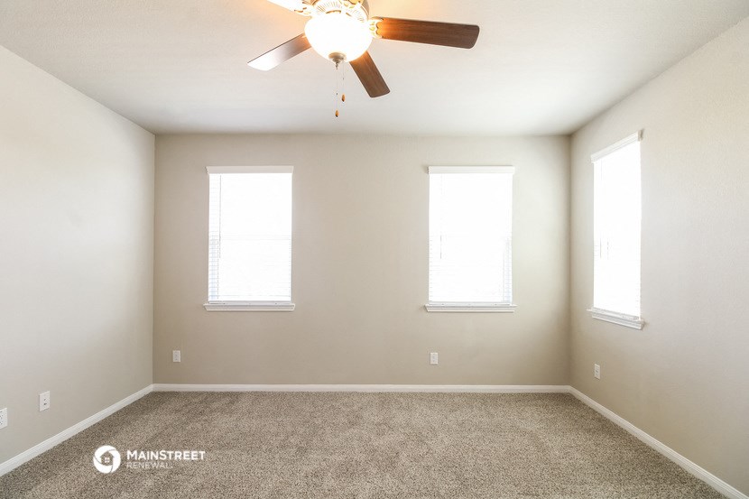 an empty room with a ceiling fan and three windows