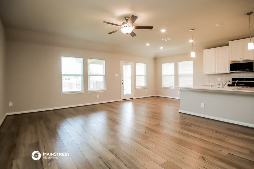 an empty living room with a ceiling fan and a kitchen