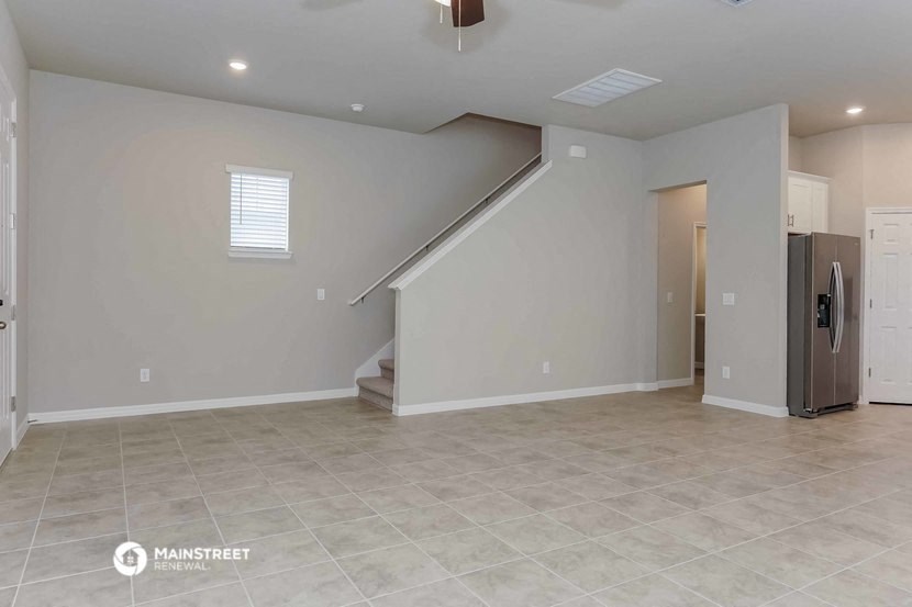 an empty living room with a refrigerator and a staircase