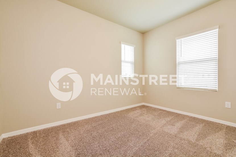 a bedroom with beige carpet and two windows