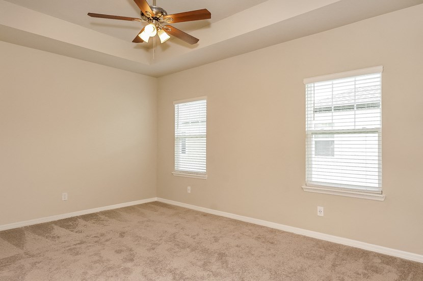 an empty living room with a ceiling fan and two windows