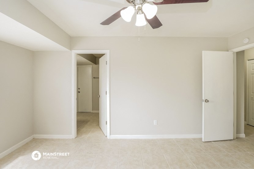 an empty living room with a ceiling fan and a hallway