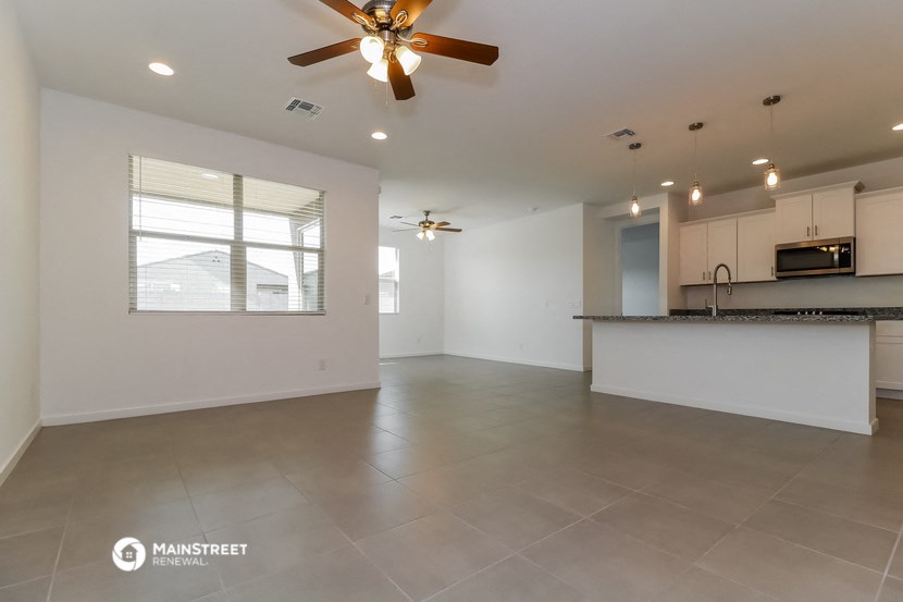 an empty living room with a ceiling fan and a kitchen