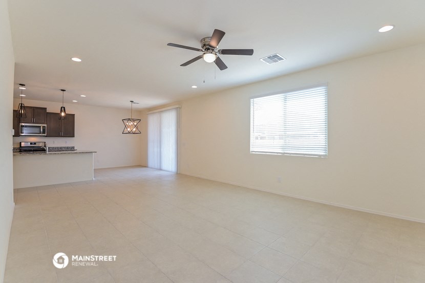 an empty living room with a ceiling fan and a kitchen