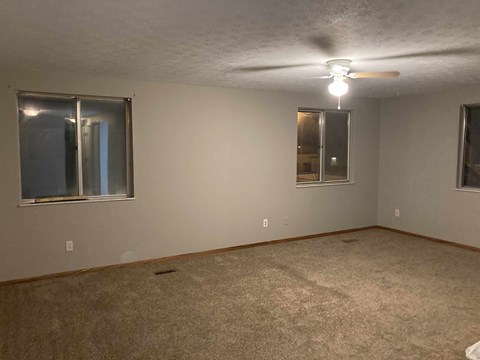 an empty living room with two windows and a ceiling fan