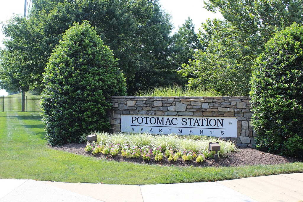 a sign for potomac station apartments in front of trees and bushes