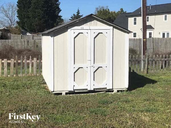 a small white shed in the grass next to a fence