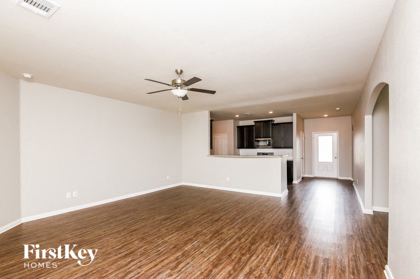 an empty living room with a ceiling fan and a kitchen