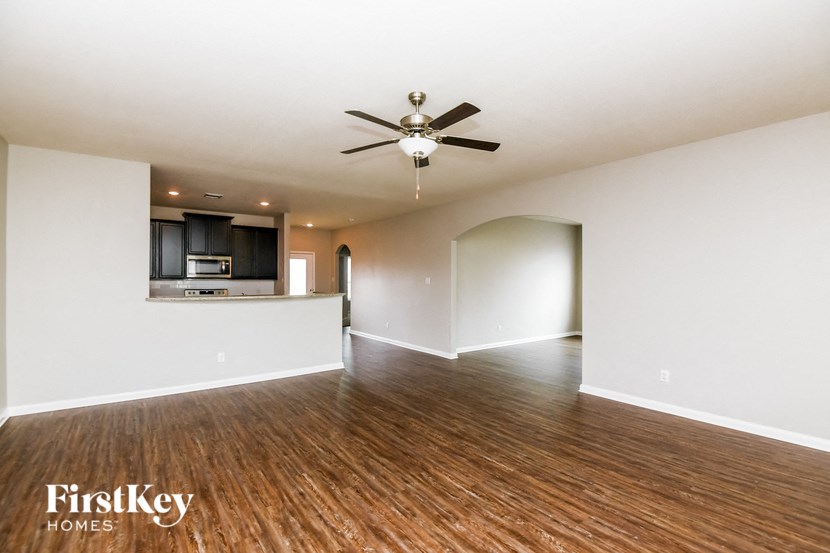 an empty living room with a ceiling fan and a kitchen