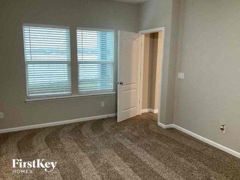 A room with a carpeted floor, two windows with blinds, and a door leading to another room.