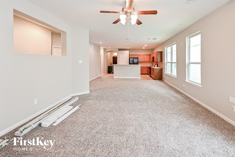 A spacious living room with a ceiling fan and a kitchen in the background.