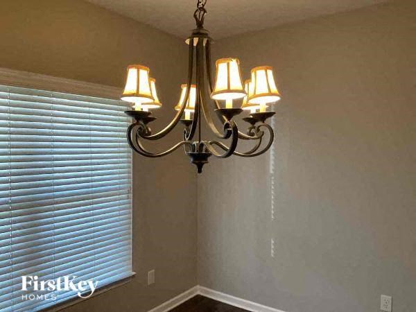 A chandelier with six lights hangs from the ceiling in a room with a window covered in blinds.
