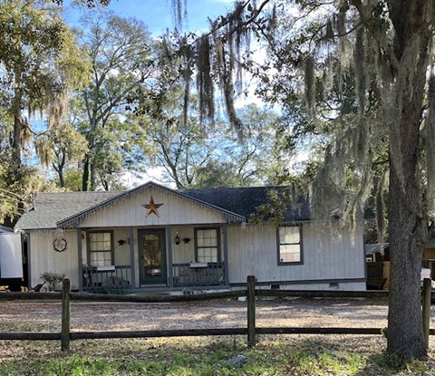 A white house with a star on the roof is surrounded by trees with Spanish moss hanging from them.