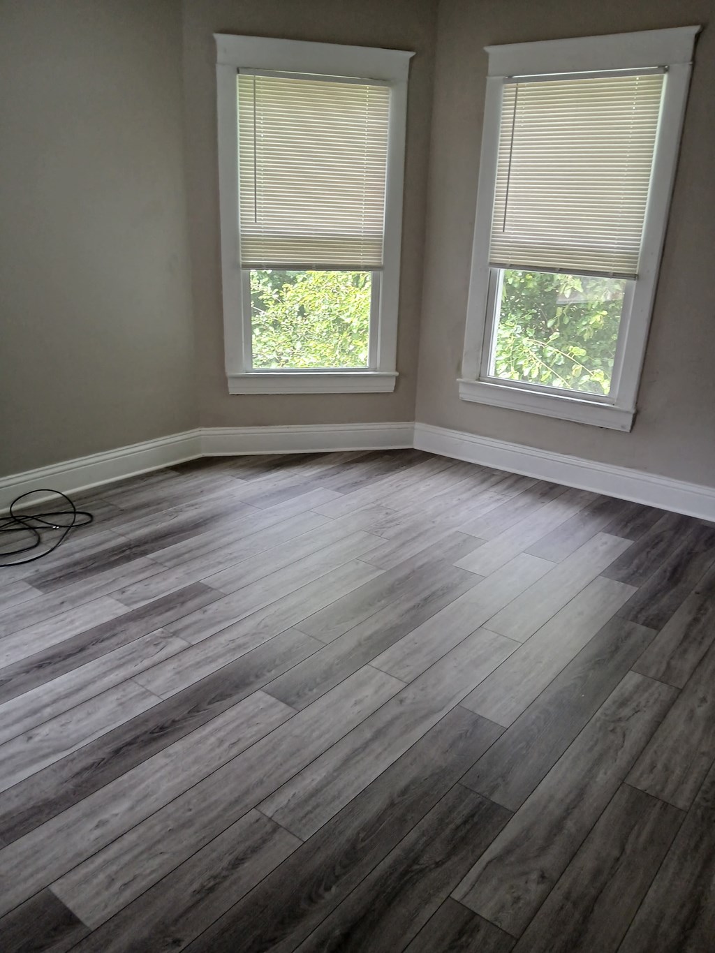 an empty room with wooden floors and two windows