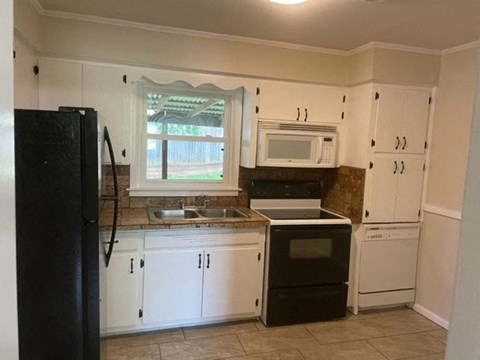 A kitchen with white cabinets and a black refrigerator.