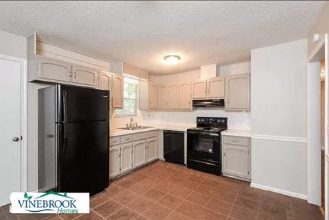 A kitchen with a black fridge and white cabinets.