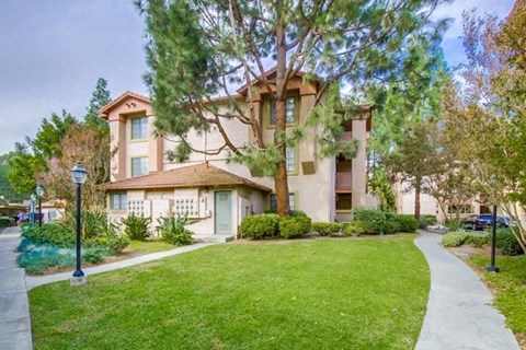 a house with a sidewalk in front of a lawn and trees