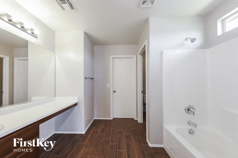 A white bathroom with a wooden floor and a large tub.