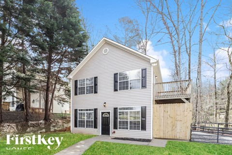 A house with a grey siding and a black door is surrounded by trees.