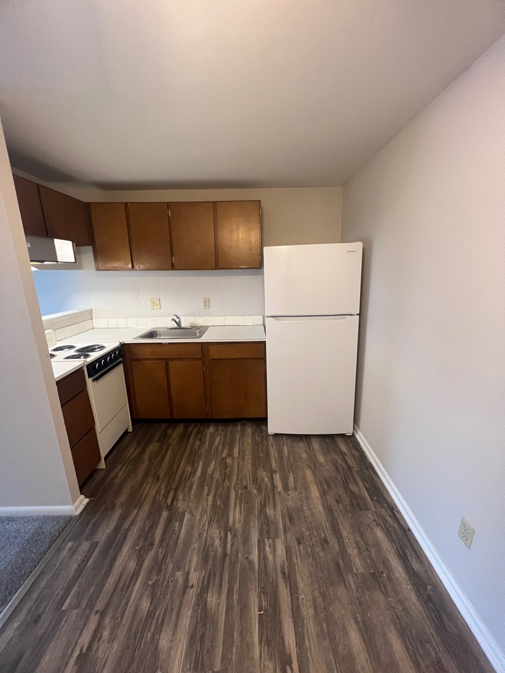 an empty kitchen with white appliances and wood floors