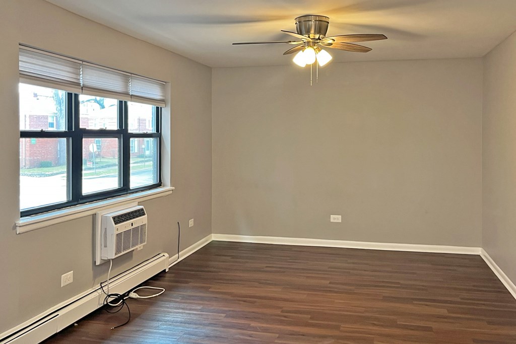 A room with a ceiling fan and a window with an air conditioner unit.