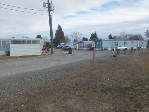 A gravel road with a white car and a white van parked on the side.