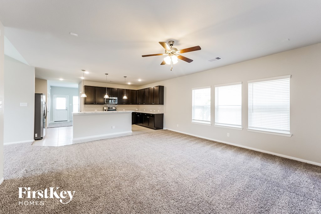 A spacious living room with a ceiling fan and a kitchen area in the background.