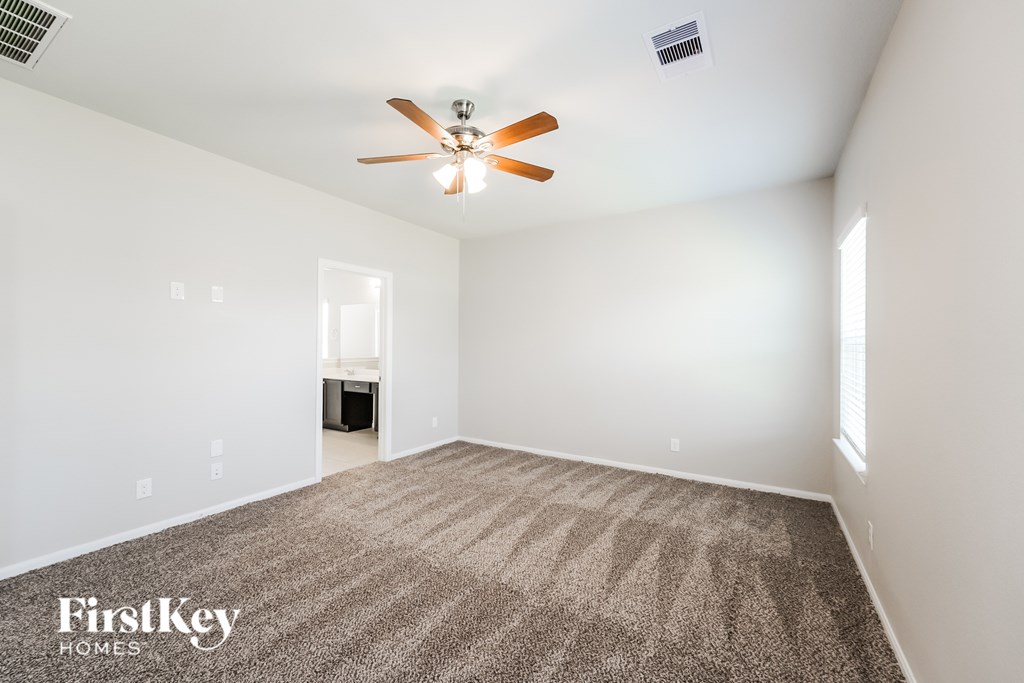 A carpeted room with a ceiling fan and a window.