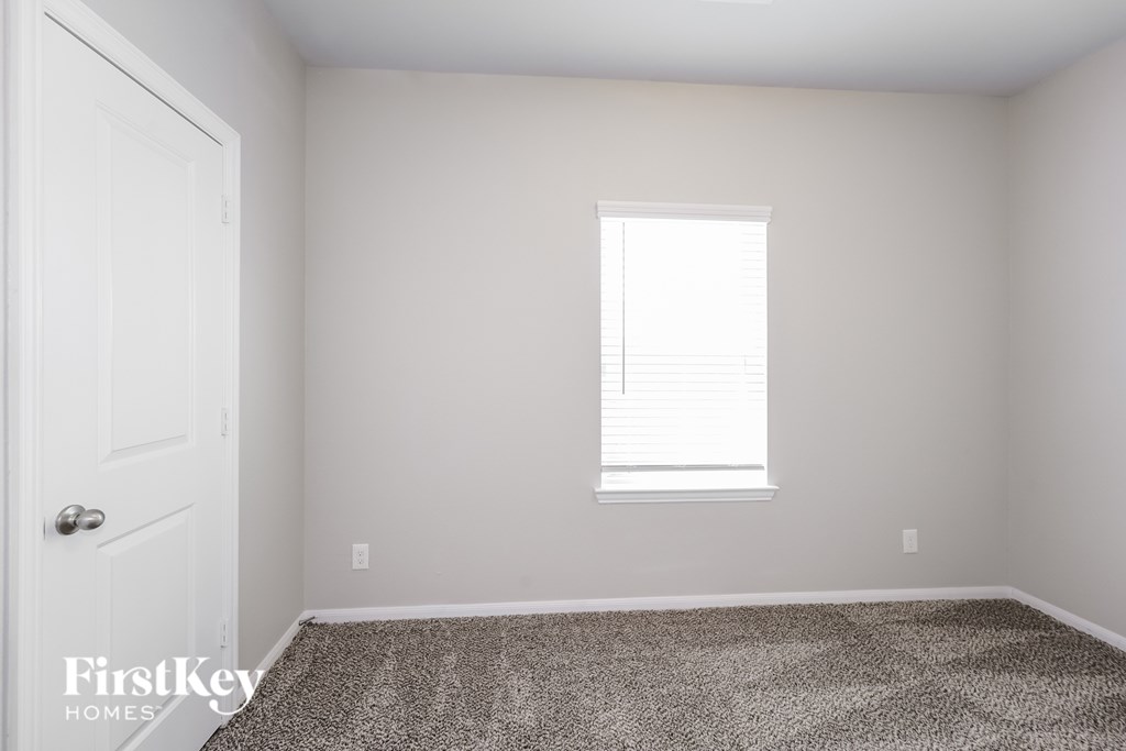 A room with a carpeted floor, a door, and a window with blinds.