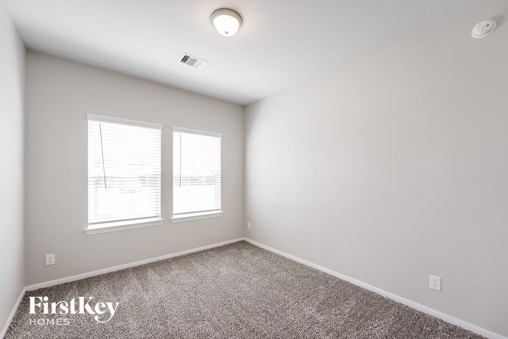 A room with a carpet floor, two windows, and a ceiling light.