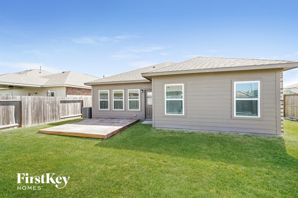A house with a brown roof and a grey siding is shown with a wooden deck in the front yard.