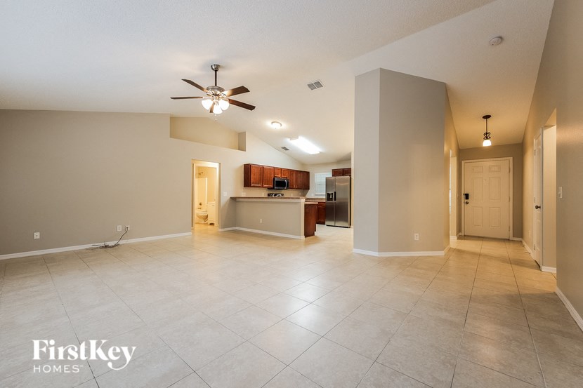 A spacious living room with a kitchen in the background and a ceiling fan in the middle of the room.