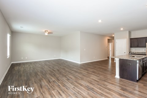 A spacious room with wooden flooring and a kitchen area in the background.