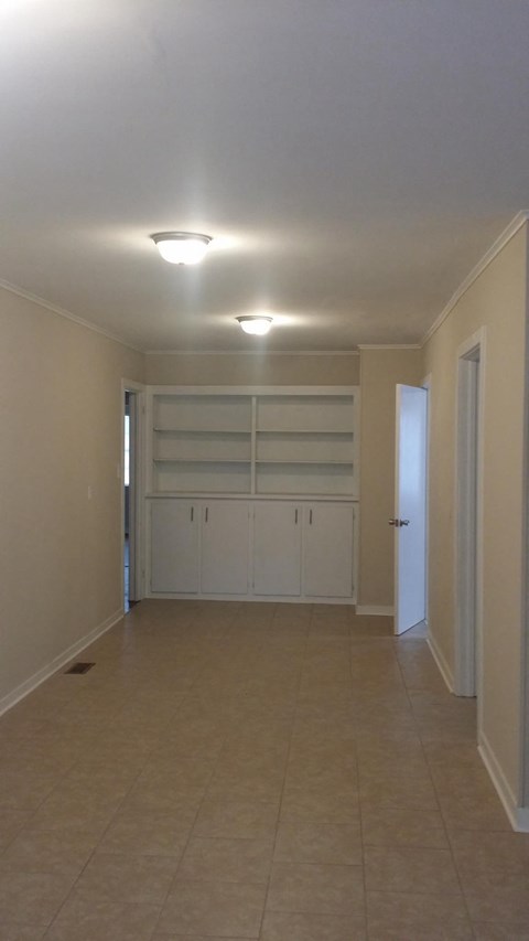 an empty living room with a tile floor and a wall with white shelves