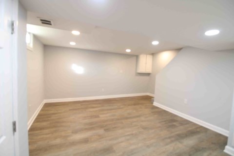 an empty basement room with white walls and wood flooring