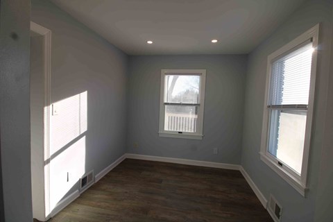 an empty room with two windows and a wooden floor
