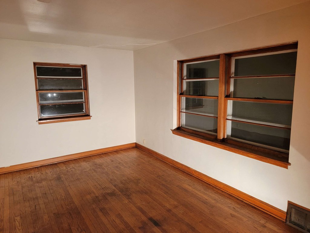 an empty room with two windows and a wooden floor