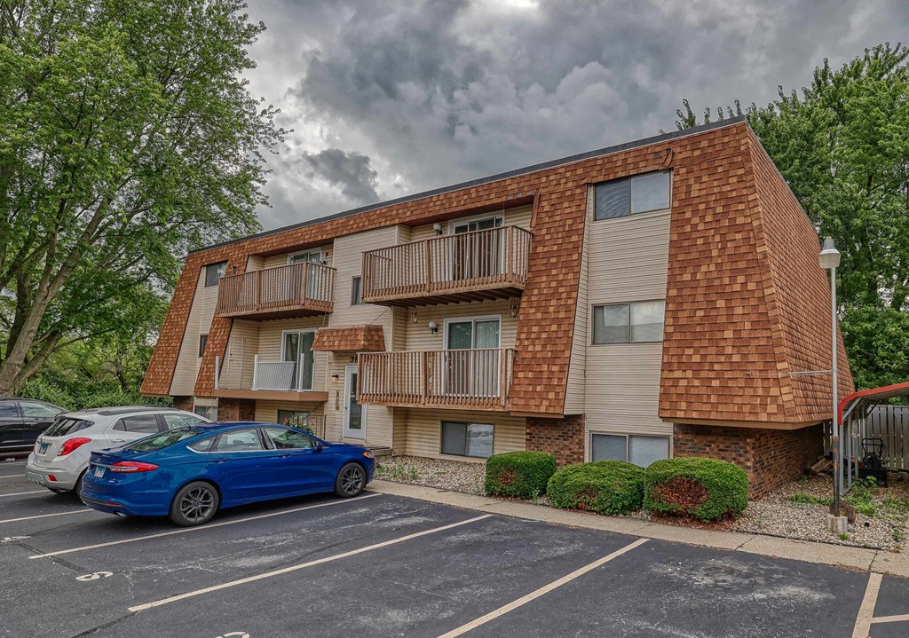 A blue car is parked in a parking lot in front of a brick apartment building.