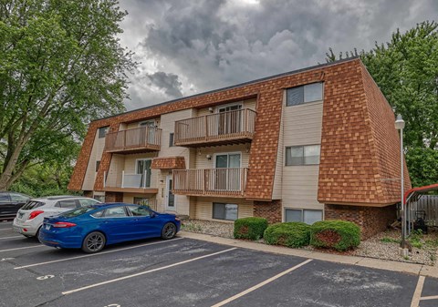 A blue car is parked in a parking lot in front of a brick apartment building.