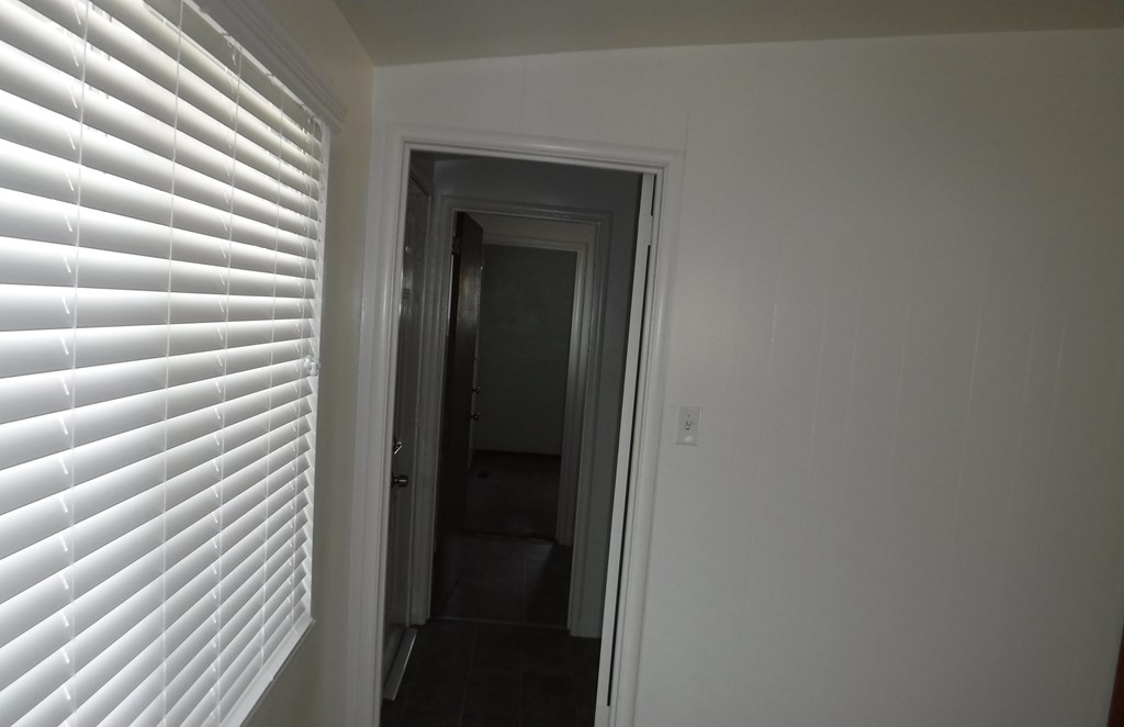 the view of the hallway from the living room through the window blinds
