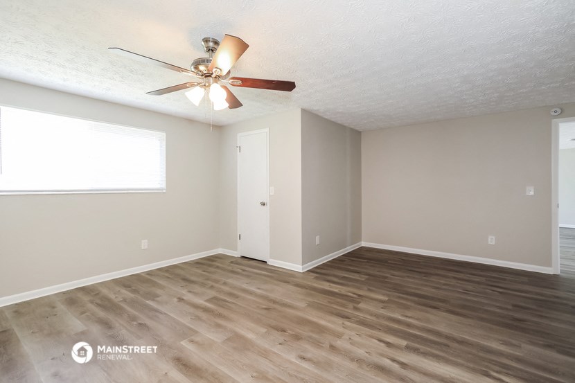 the spacious living room with wood flooring and a ceiling fan