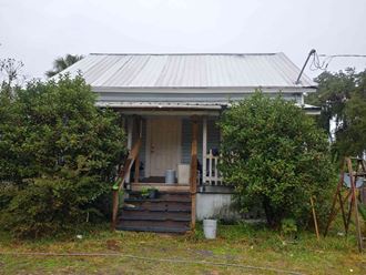 the front of a small house with stairs and a tin roof
