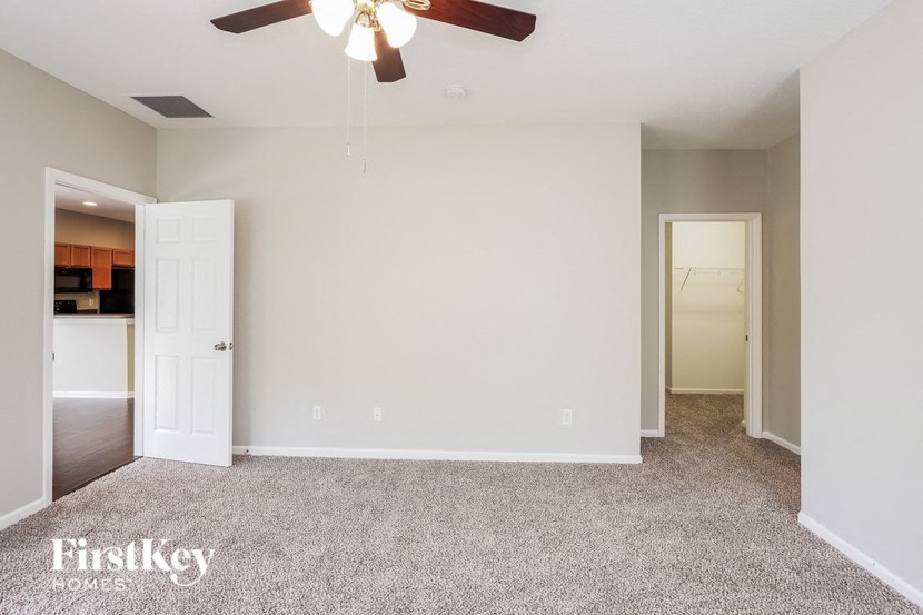 a empty living room with a ceiling fan and a door to a kitchen