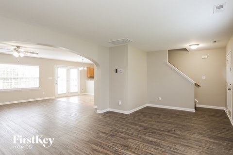 A spacious room with wooden flooring and a staircase on the right side.