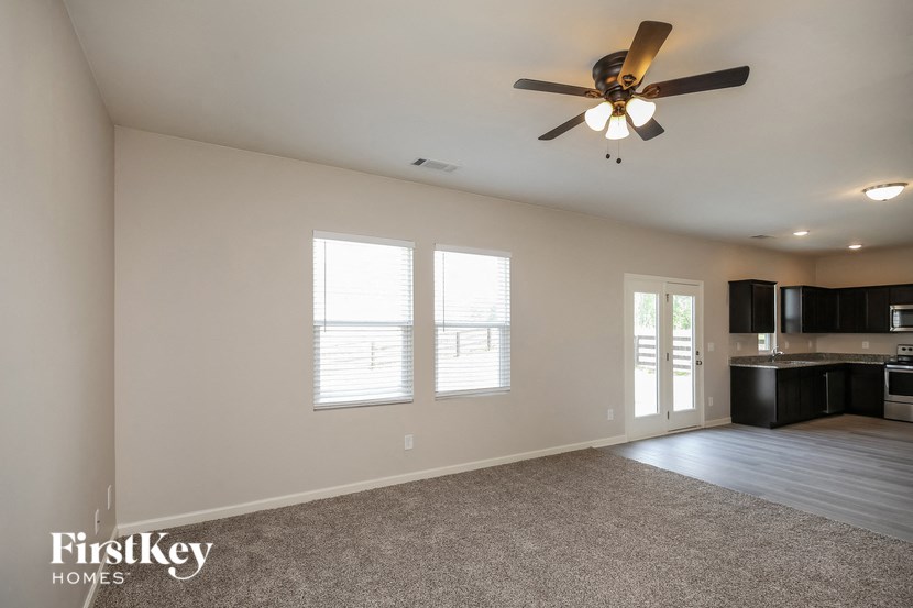 a empty living room with a ceiling fan and a kitchen
