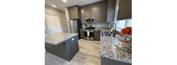 Modern kitchen with granite counters, stainless appliances, wood floors, and window above sink.